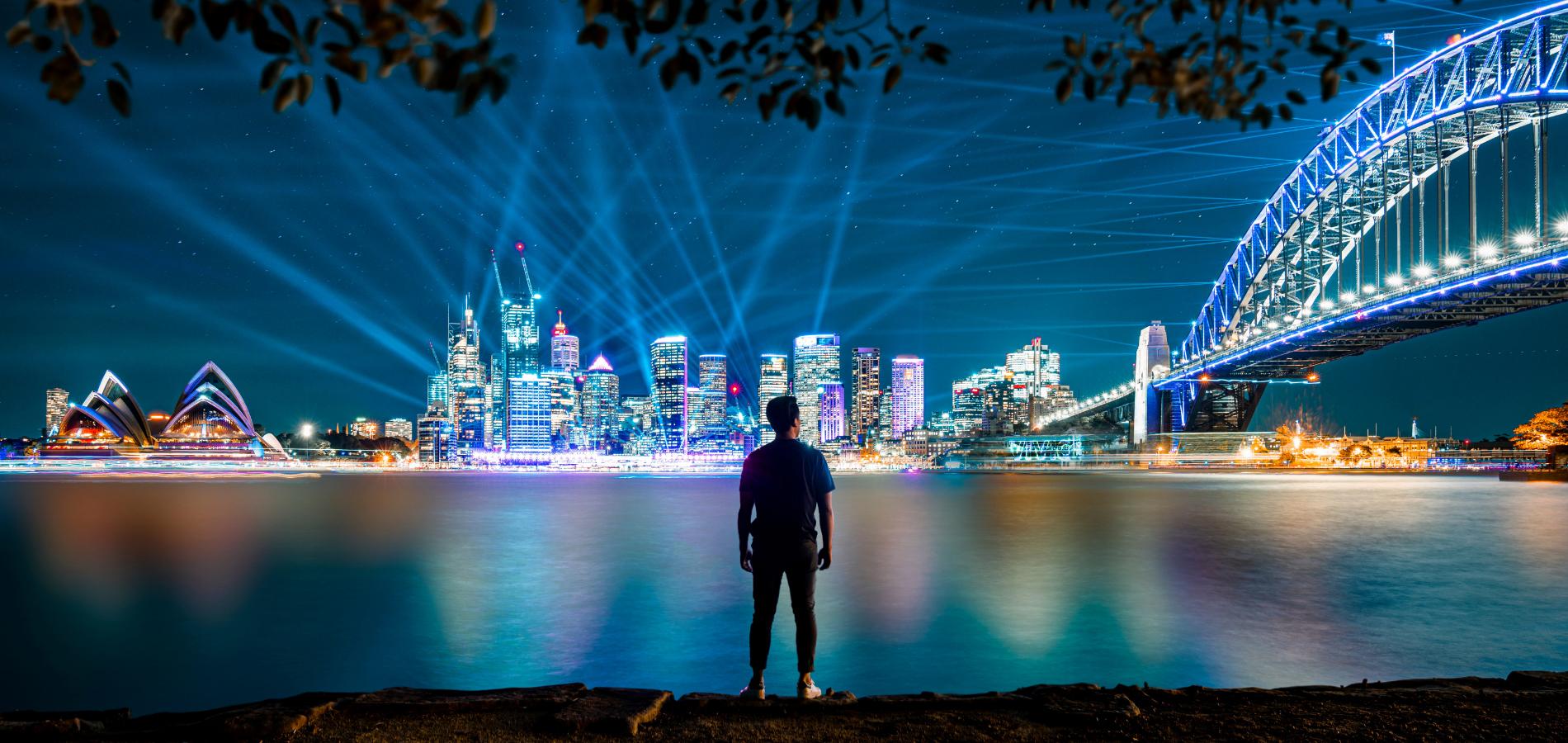 Person standing in front of Sydney Harbour during Vivid Sydney in the evening